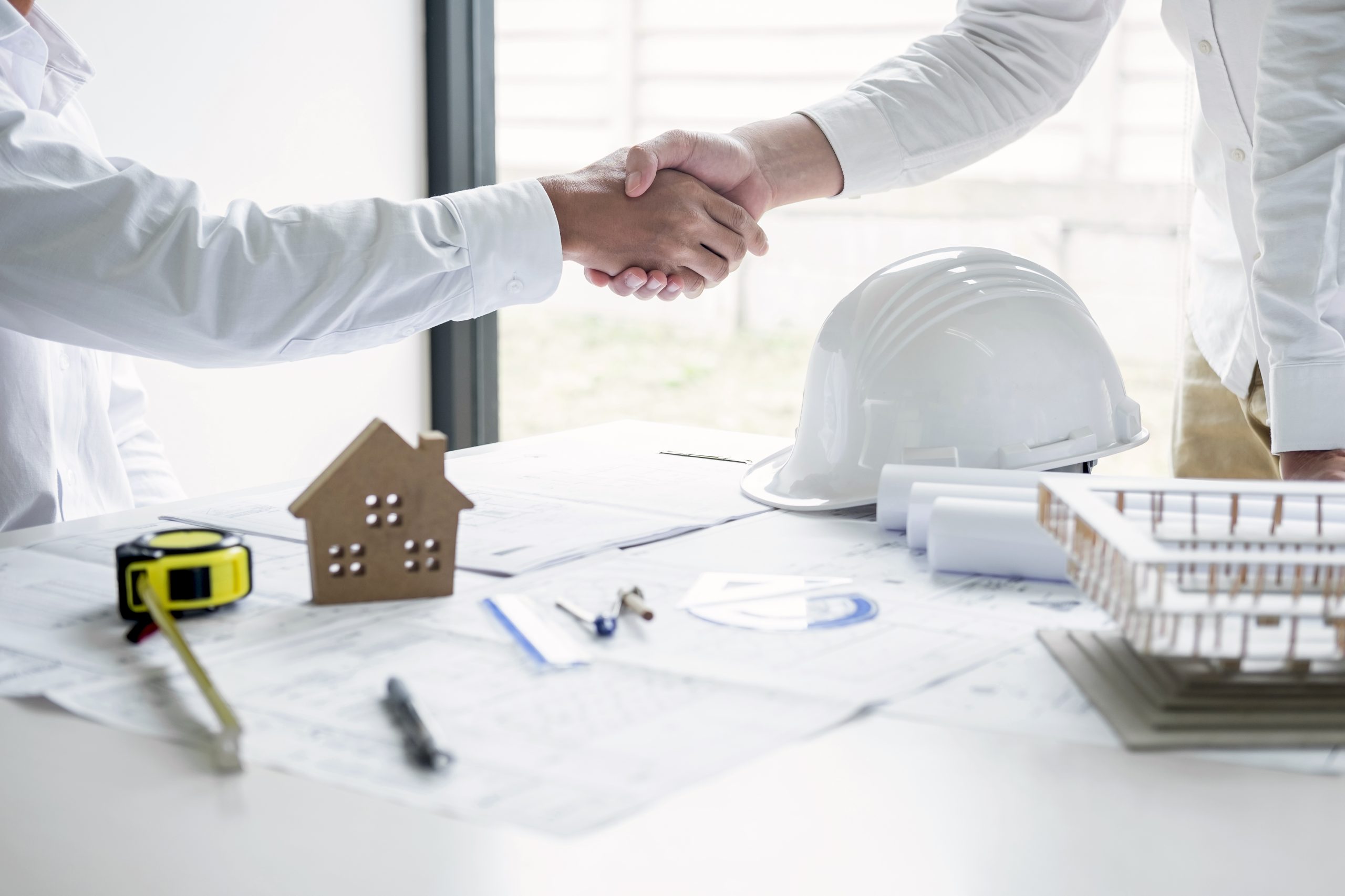 Handshake of collaboration, Construction engineering or architec Handshake of collaboration, Construction engineering or architect discuss a blueprint and building model while checking information on sketching, meeting for architectural project of partner.